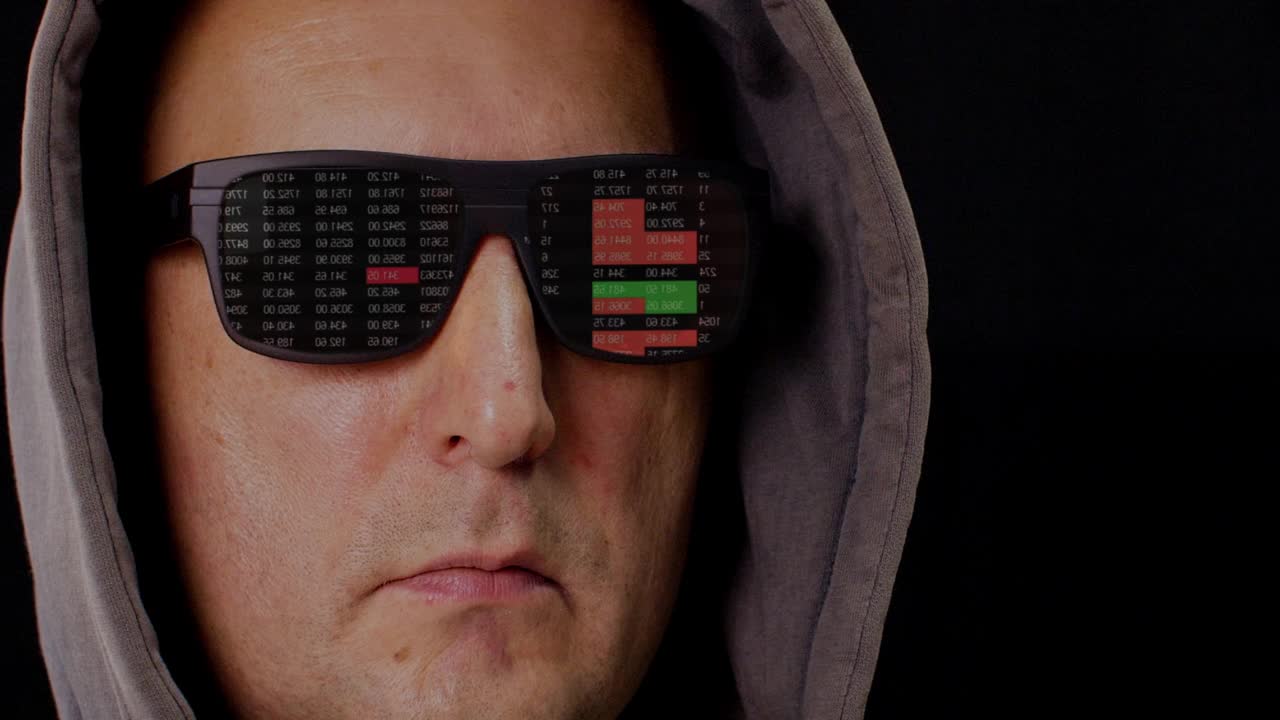 近距离观察蒙面男子和黑色VR眼镜与反射交易交易数据。证券交易所里映着黑色墨镜的男子戴着兜帽，孤立在黑暗的背景下