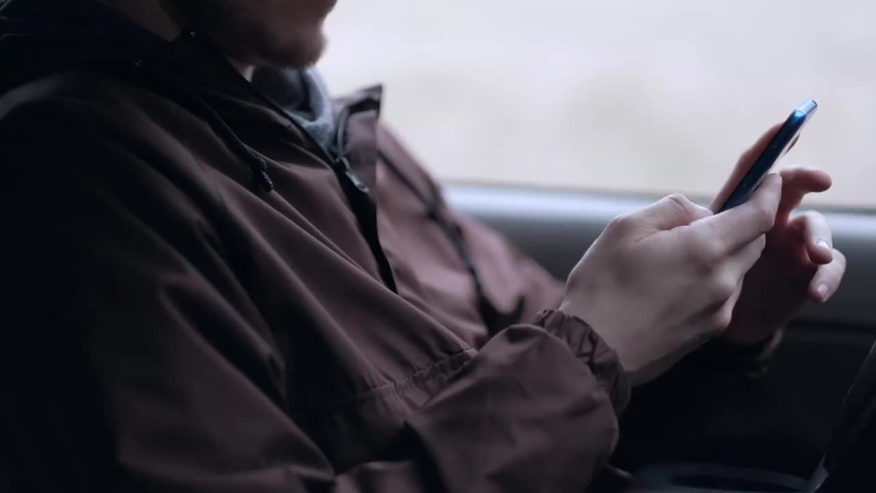 一名年轻人坐在汽车的驾驶室里，正在使用智能手机
