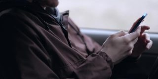 一名年轻人坐在汽车的驾驶室里，正在使用智能手机