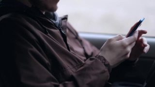 一名年轻人坐在汽车的驾驶室里，正在使用智能手机视频素材模板下载