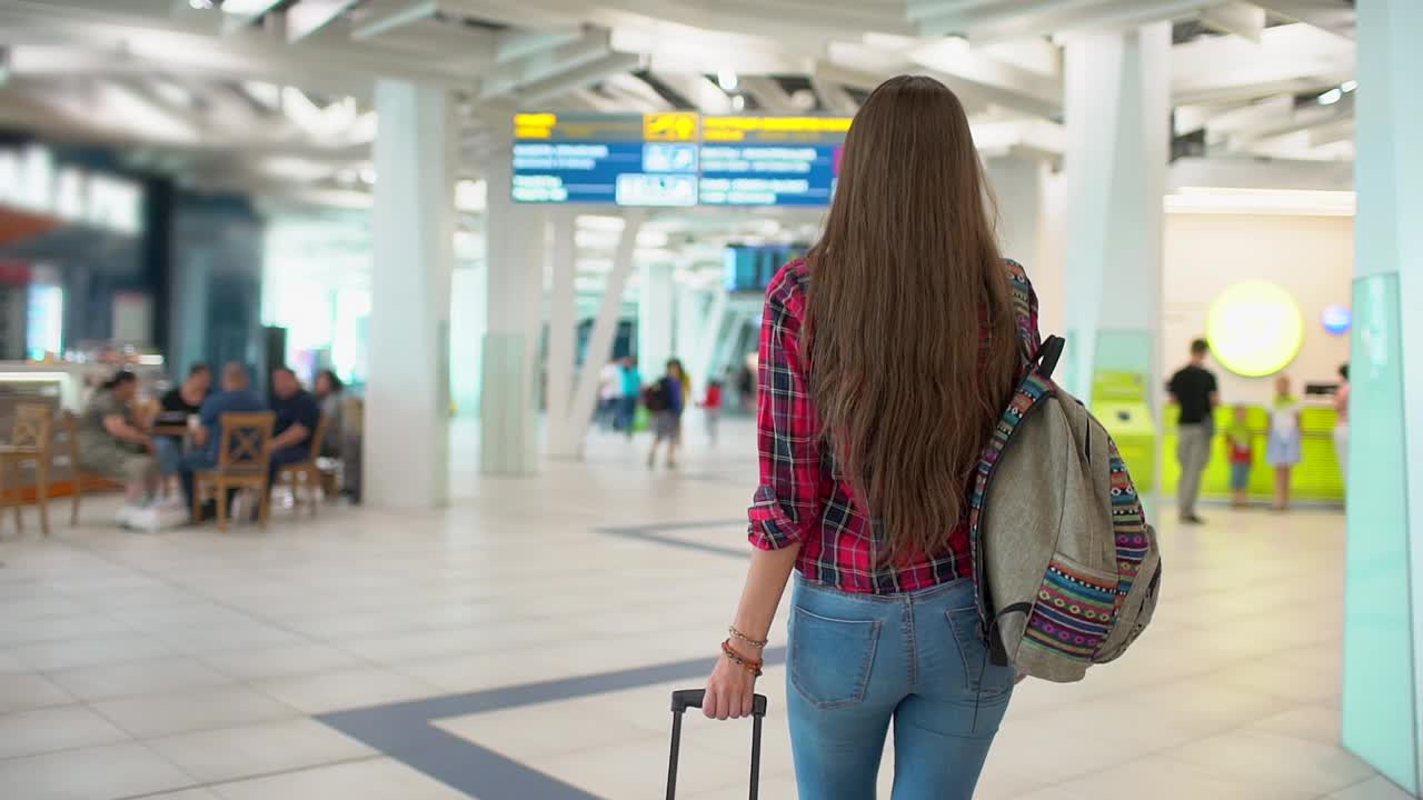 年轻的女旅客穿着休闲衬衫和行李走在现代化的机场航站楼