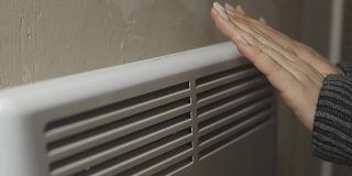 一个俄罗斯女人正在一个寒冷的房子散热器取暖自己，与供暖的问题，加热房间与一个电对流