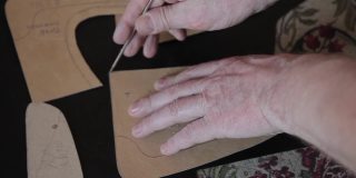 这名男子的手是一个裁缝皮匠在一块天然皮革上标记了一个图案。手工制作的皮革生产。手工作坊桌上的图案