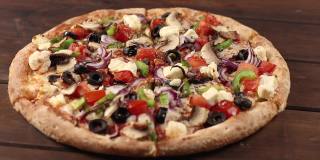 整个新鲜的圆披萨，鸡肉，蔬菜，蘑菇和奶酪在木制的棕色桌子上旋转。披萨店的美味快餐背景