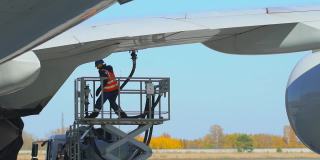 机场飞机机组加油由航空公司地面技术人员维护。飞机准备起飞，飞机维修人员在飞机机翼上、楼梯上使用燃油软管