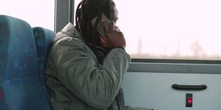 一名戴着面具的黑人在公交车窗口边打电话，把电话放在耳边