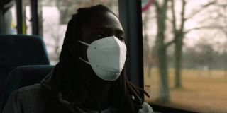 画像靠近车窗的黑人男子在公交车上戴着面罩，正对着乘客的脸
