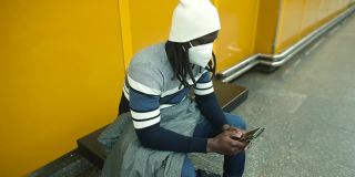 戴面具的非洲人手里拿着电话他坐在火车站的长凳上。