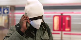 非洲乘客戴着面具打电话。他在耳边使用小工具，听信息