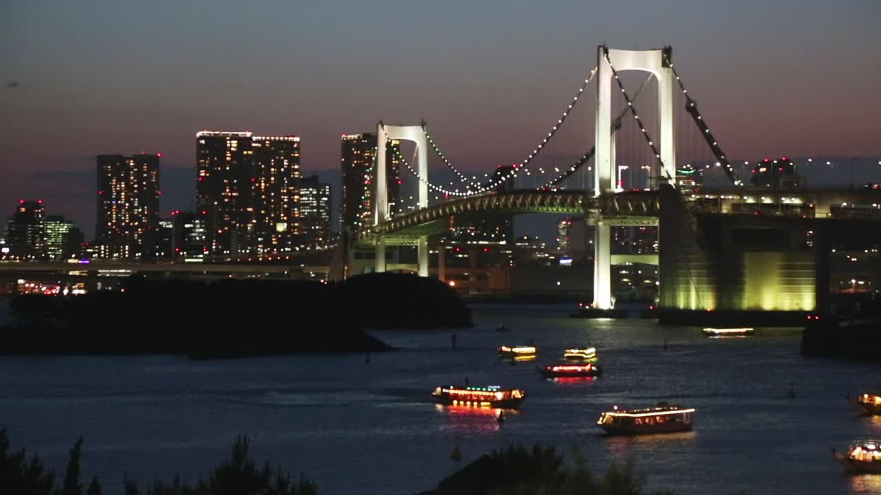 描述日落时分的东京全景天际线，彩虹桥和一些船只漂浮在东京湾上