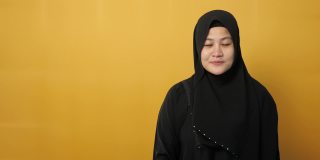 亚洲穆斯林妇女微笑，指着展示在她的一边，以黄色背景与复制空间
