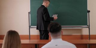 大学里的老师站在黑板旁边和学生们谈话。