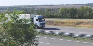 卡车在高速公路上行驶。卡车围绕着田野和树木在高速公路上行驶