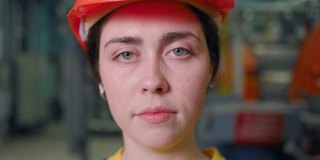 一个年轻的女工程师的肖像，她脱下她的保护头盔和微笑。镜头从脸部的移动。现代工业和制造业