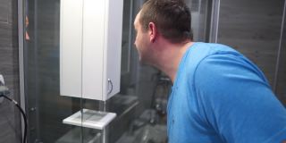 一名身穿t恤的男子在浴室的镜子前用理发器给自己理发，在隔离冠状病毒大流行的冠状病毒19，呆在家里的概念