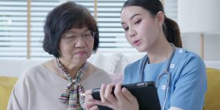 年轻的亚洲女性护士，辅助生活，家庭护理员或医生在家里拜访老年人，在平板电脑上在线谈论结果跟踪检查表，保健建议或处方。