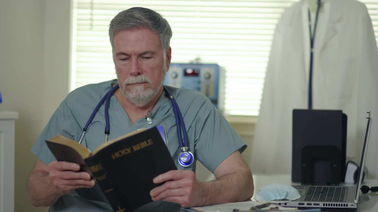 在一个小诊所里，一位基督教医生坐在他的办公桌前阅读《圣经》，以寻求鼓励和安慰。