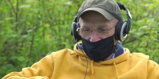 一位戴口罩的老人使用耳机在互联网上讲话