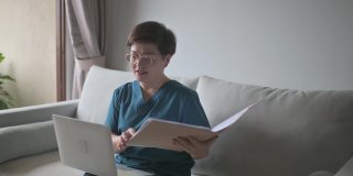 亚裔华裔女医生在家工作，在客厅用笔记本电脑咨询她的成年病人