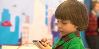 可爱的小男孩在用智能手机。在第四届俄罗斯科学节上为儿童展示的机器人。该活动旨在普及科学和展示技术进步。可爱的小男孩在玩电子玩具机。情感、兴趣