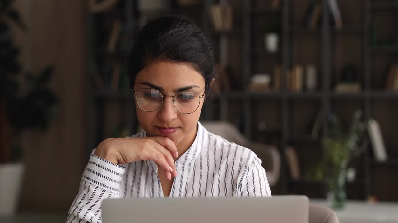 沉思的年轻印度女商人戴着眼镜在笔记本电脑上工作。