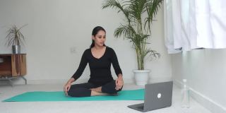 一个亚洲女人在笔记本电脑前做瑜珈练习。