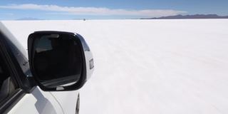 开着吉普车行驶在沙漠中明亮的白色水晶盐表面上。前景的后视镜。