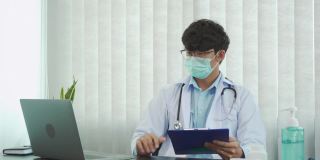 医生戴着口罩坐在办公室里用笔记本电脑工作。