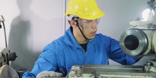 亚洲机械工人在铣床上工作。技术人员在操作机器时戴上防护眼镜和安全帽，以确保安全。这个人小心翼翼地工作以防危险。
