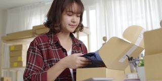 年轻有吸引力的美丽时髦的亚洲女性包装产品小商包裹订购网上零售商店交付给客户。中小企业业主工作准备dropshipping箱在家办公室。