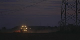 SLO MO拖拉机在夜间的电塔下犁地