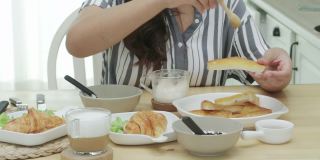 概念:一个亚洲女人在牛角面包桌上吃快餐，面包、酸奶和咖啡放在桌上就可以吃了。