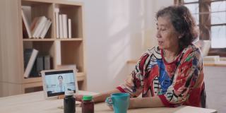 远程医疗的亚洲老年患者女性使用笔记本电脑视频电话与女医生，护士在家里的客厅