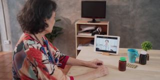 远程医疗的亚洲老年患者女性使用笔记本电脑视频电话与女医生，护士在家里的客厅