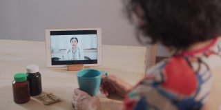 远程医疗的亚洲老年患者女性使用笔记本电脑视频通话的女医生，护士在家里的客厅