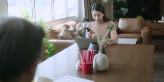 新的正常工作远程在家的概念，亚洲爸爸妈妈在家里工作与笔记本电脑智能手机在餐厅，而他的儿子正在周围玩耍，要求一起玩