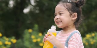 可爱的小女孩拿着一瓶橙汁在花园里喝，慢镜头拍摄。