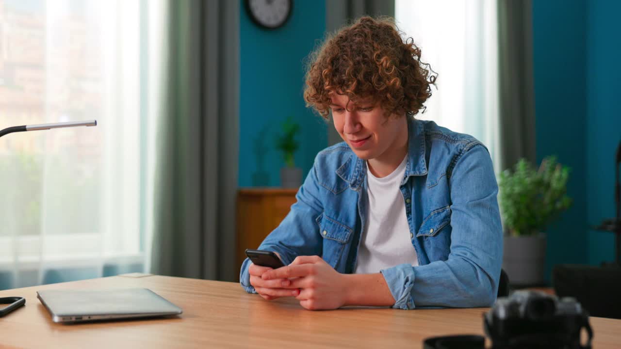 青少年在家里用智能手机发短信。帅哥花时间在社交网络上使用手机。一个打手机的白人少年。生活方式的概念