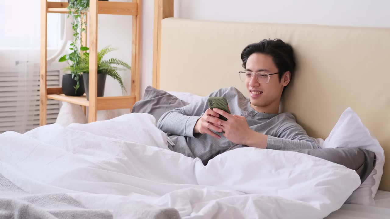 男人打呵欠和伸懒腰在床上使用手机