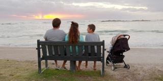 幸福的一家人坐在海边一起看日落。