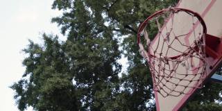 在室外的树荫下，扔出的橙色篮球干净利落地击中篮筐。击中目标。用慢动作干净利落的射门达到目标