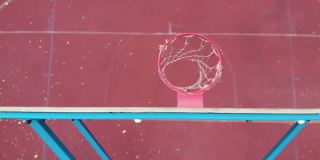 篮球篮板上方的顶角橙色球击中篮筐，在室外红色球场慢速动作中得分
