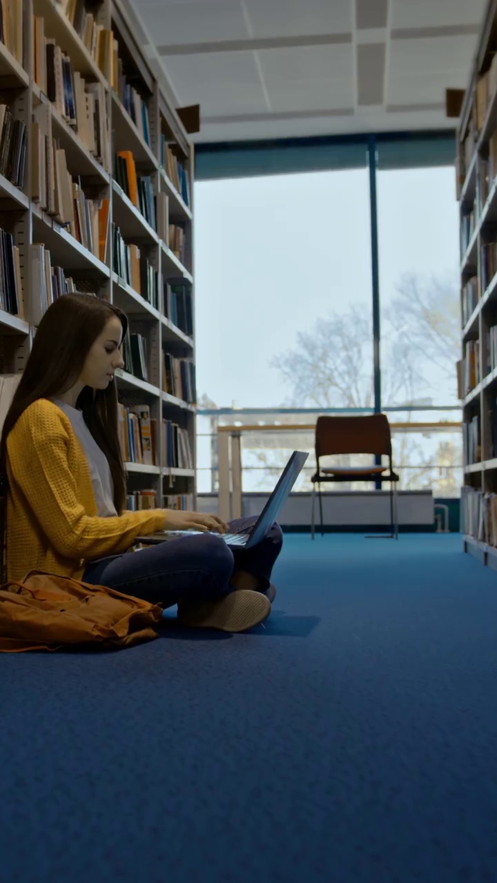 SLO MO女子使用笔记本电脑，而其他学生在图书馆的书架上找一本书