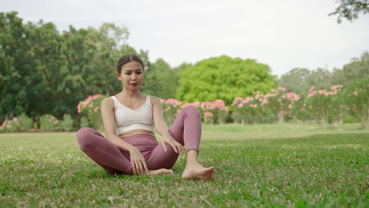 一位年轻的亚洲女子坐在花园里练瑜伽，她很放松，很享受锻炼。