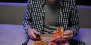 年轻的潮男吃着披萨，看着最喜欢的电视电影，在客厅的沙发上放松。吃意大利菜的男人。放松影院频道休息