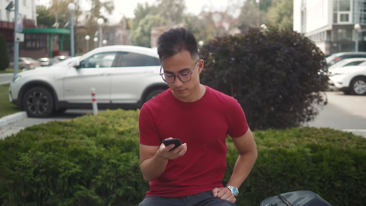 英俊的亚洲商人正在使用智能手机和耳机，与朋友交谈时，蓝牙耳机音频信息语音识别，人工智能助手