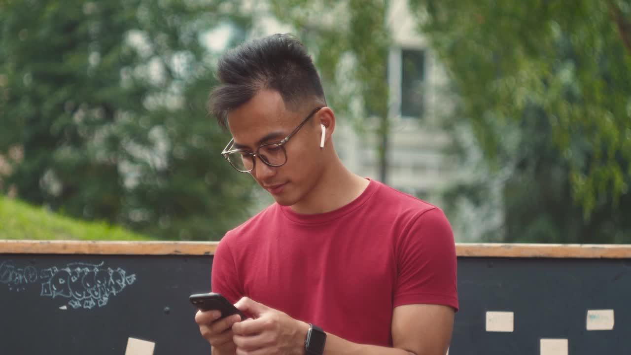 英俊的亚洲商人正在使用智能手机和耳机，与朋友交谈时，蓝牙耳机音频信息语音识别，人工智能助手
