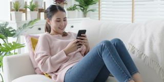 年轻迷人美丽随意的亚洲女性在沙发上看手机玩社交媒体