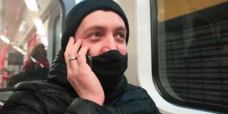 蒙面男乘客在地铁车厢里打电话。他把小玩意儿放在耳朵上。