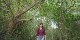 一个年轻的亚洲女人独自在森林里旅行。女孩在大自然中感受着清新、美妙、刺激和放松，环顾四周的风景，然后继续快乐地散步。